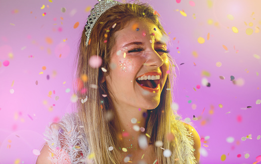 Carnaval Brazil. Excited and Cheerful. Throwing confetti. Face of young woman with colorful makeup, dressed up for fun. Bright background. Party concept, celebration and festival.