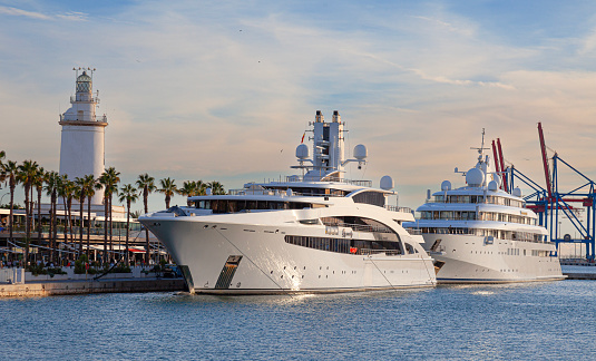 Málaga, Spain - 30th October 2023: The superyachts iDynasty and Golden Odyssey tied up at Muelle Uno in Málaga, Costa del Sol, in front of the Farola de Málaga (lighthouse)