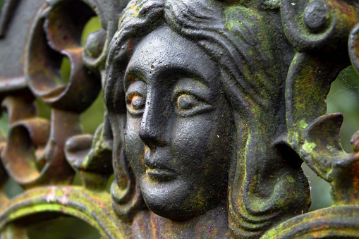 Image of a female face among filigrees located on the back of a wrought iron bench in the garden of the Pazo do Faramello