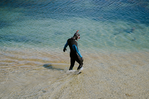 Serene moment as a beachgoer wades into crystal-clear waters, eager to snorkel and discover the ocean's hidden treasures.