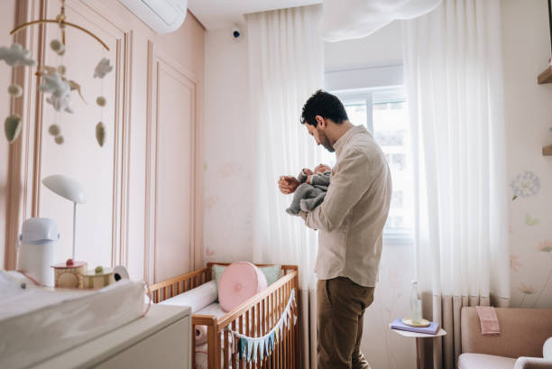 father holding his newborn daughter at bedroom - padres-amos-de-casa-ilustraciones fotografías e imágenes de stock