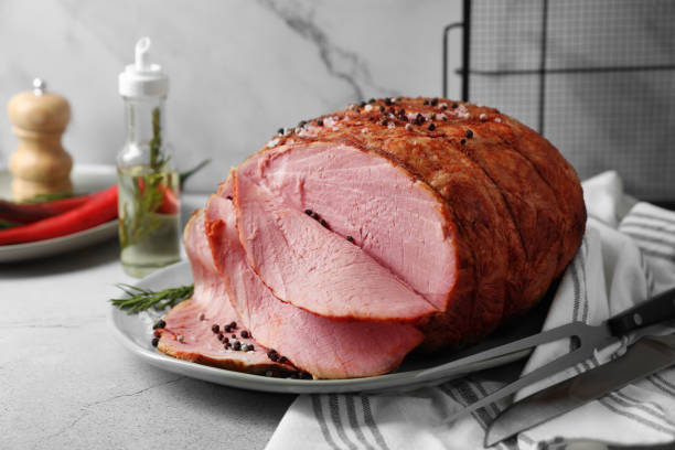 istock Delicious baked ham, carving fork and knife on light grey table 1892967287