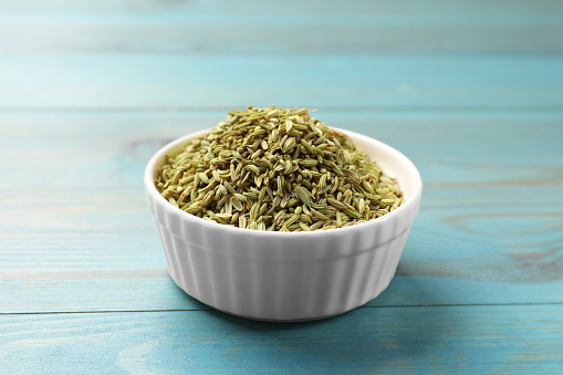 Fennel seeds in bowl on light blue wooden table, closeup