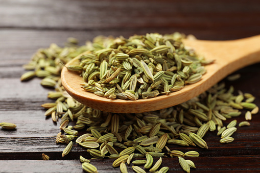 Spoon with fennel seeds on wooden table, closeup