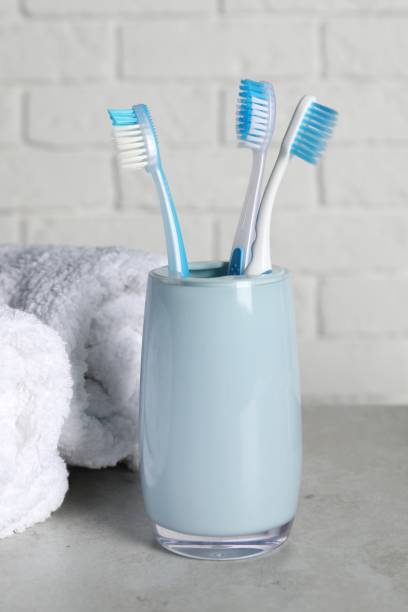 istock Plastic toothbrushes in holder and towels on light grey table 1893228746
