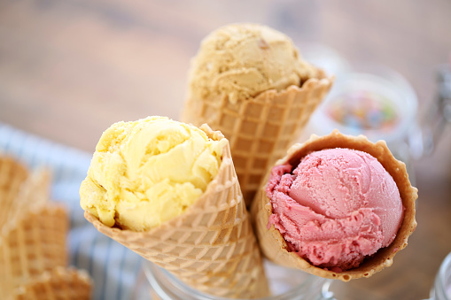 Summer ice cream buffet with a variety of ice cream flavors and sweet toppings. Overhead view table scene on a rustic white wood background.