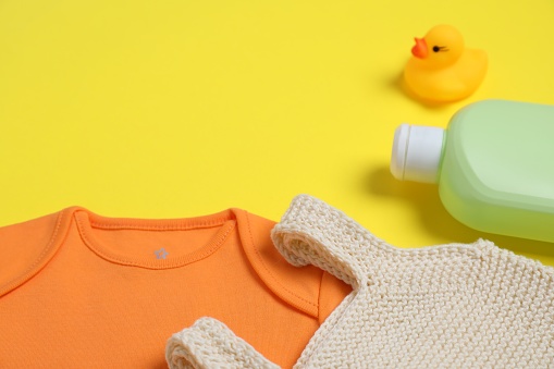 Bottles of laundry detergents, baby clothes and rubber duck on yellow background. Space for text