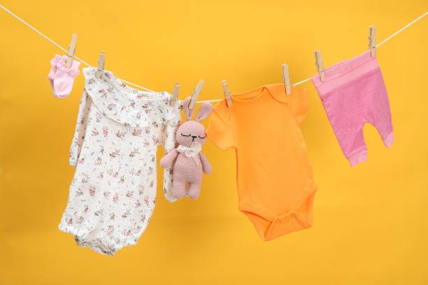 istock Different baby clothes and bunny toy drying on laundry line against orange background 1893265839