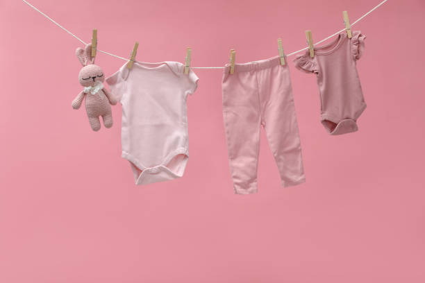 istock Different baby clothes and bunny toy drying on laundry line against pink background 1893265841