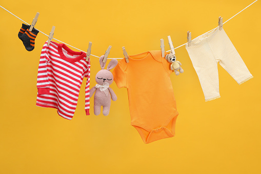 Different baby clothes and toys drying on laundry line against orange background