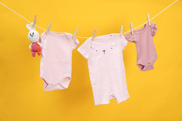 istock Different baby clothes and bunny toy drying on laundry line against orange background 1893266374
