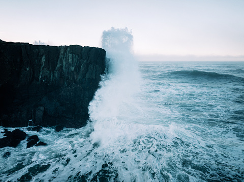 Black and white powerful ocean waves crashing against rocky coastline