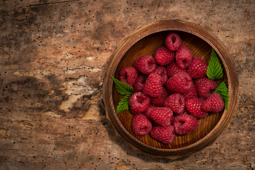 Juicy, delicious raspberries in a wooden bowl, on a wooden background. From above, with copy space