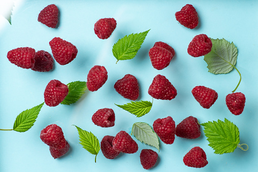 Ripe, juicy raspberries with green leaves on pastel blue background pattern