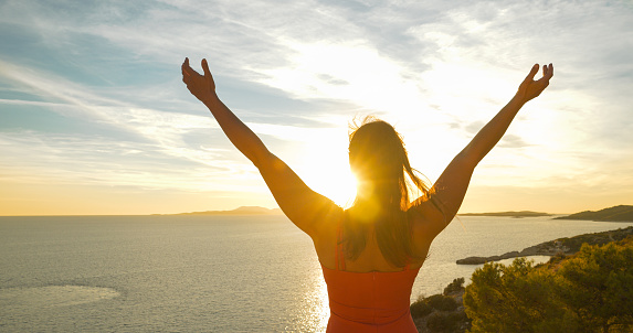 LENS FLARE, CLOSE UP: Beautiful tourist embraces gorgeous golden sunset on Hvar. She is admiring stunning view and watches last rays of summer sun gently spilling over picturesque Dalmatian seascape.