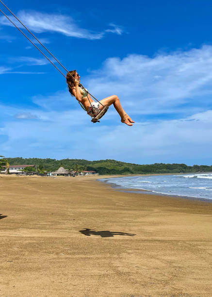 istock LOW ANGLE VIEW: Young lady enjoying on a beach swing with view of Pacific Ocean 1893306087