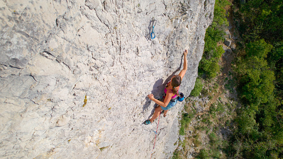 CLOSE UP: Pretty lady lead climbing a challenging route in steep limestone wall. She is advancing on a sharp end of rope along the climbing route in limestone wall. Incredible area for rock climbing.