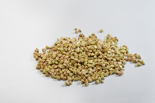 Small heap of uncooked buckwheat on a light gray background, high protein and gluten free food used for groats and porridge or as an ingredient in baked goods, copy space, selected focus