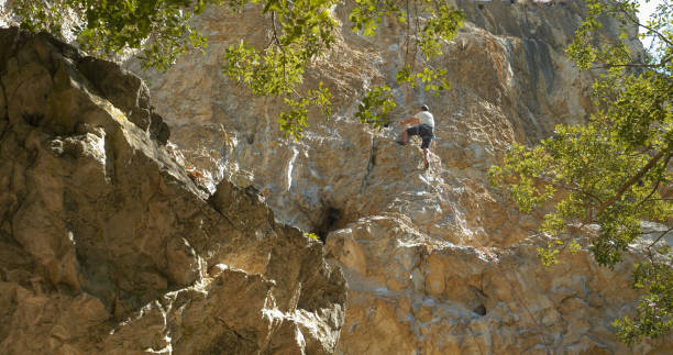 low angle view: lead climber climbs limestone wall and attaches belay equipment - quickdraw zdjęcia i obrazy z banku zdjęć