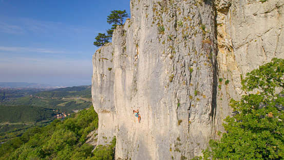 Solutré-Pouilly, France – September 13, 2017: photography showing an adult man (in the middle) climbing on the Rock of Solutré, a limestone escarpment and an iconic site of the Saône-et-Loire, in the south of the Bourgogne in France. The photography was taken from a small town in the countryside, near the city of Mâcon, France.