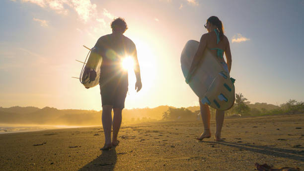 istock LENS FLARE: Surfers carry surfboards on a tropical sandy beach in golden light 1893318461