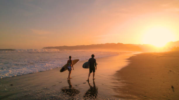 istock AERIAL: Surfers watch big breaking waves from beach after sunset surf session 1893318972
