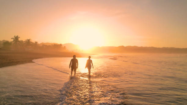 istock AERIAL: Tidal wave washes on sandy beach and crosses path of two walking surfers 1893318980