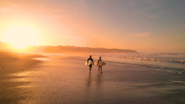 istock AERIAL: Young couple walking on beautiful sandy beach after sunset surf session 1893318982