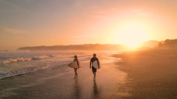 istock AERIAL: Cheerful surfers admire big waves while walking on sandy shore at sunset 1893318989