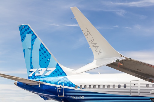 The image shows the right side of the aft fuselage and tail of a Boeing 737 MAX 10.  The aircraft has a perfectly blue sky as a stunning backdrop.   The new technology scimitar winglet  is clearly seen in the image with the lower part of the winglet pointing at the \