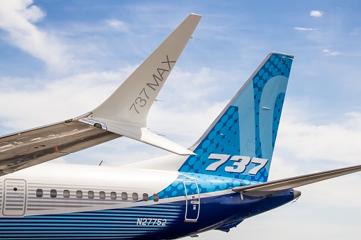 The image shows the aft fuselage and tail of a Boeing 737 MAX 10.  The aircraft has a perfectly blue sky with wispy clouds as a stunning backdrop.   The new technology scimitar winglet  is clearly seen in the image with the lower part of the winglet pointing directly at the \