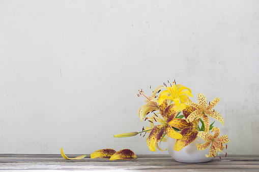 yellow lily in ceramic white vase on wooden table