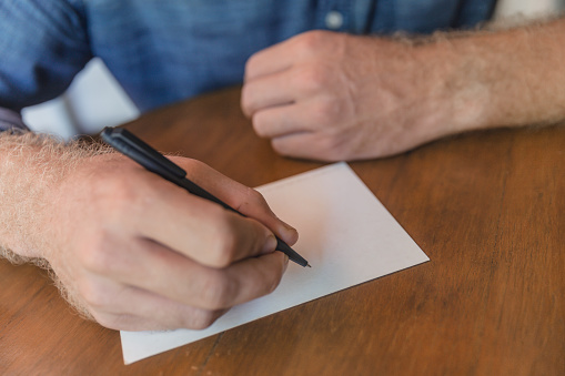 Close-up shot of unrecognizable man writing a postcard for his family during business trip