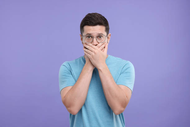 istock Embarrassed man covering mouth on purple background 1893377633