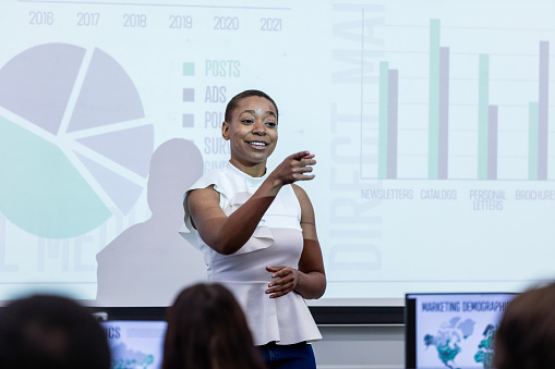 The young adult businesswoman gestures to an unseen seminar attendee during her lecture.