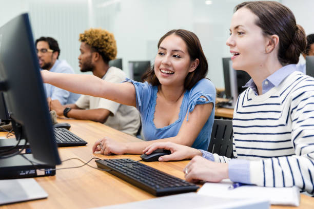 istock Female tutor helps young female student in college computer lab 1893496073
