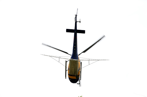 Electrical workers high above the ground building a high voltage utility tower, about to be picked up by a helicopter.