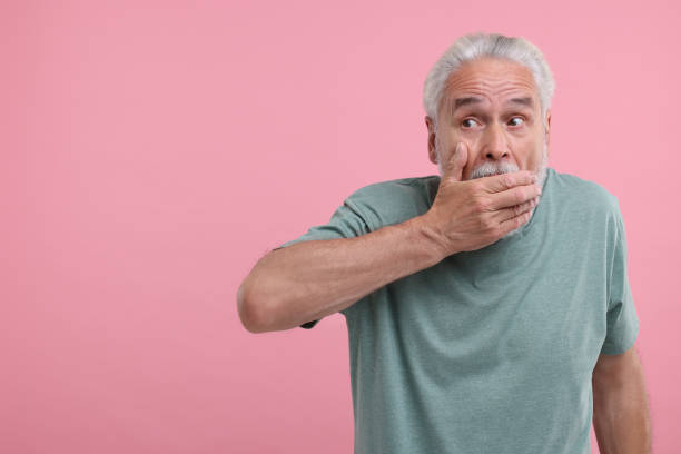 istock Embarrassed senior man covering mouth on pink background. Space for text 1893512287