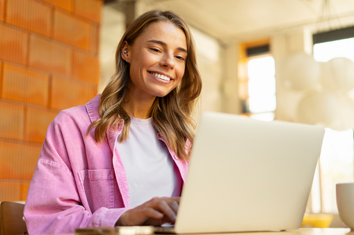 Portrait smiling beautiful woman using laptop computer in modern office. Happy copywriter typing on keyboard working freelance project. Technology, successful business concept