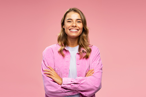 Portrait of attractive smiling woman, smart happy university student holding arms crossed looking at camera isolated on pink background. Education concept