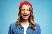 Closeup portrait smiling American woman winks wearing stylish red hat isolated on blue background