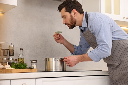 Man tasting delicious soup with spoon in kitchen