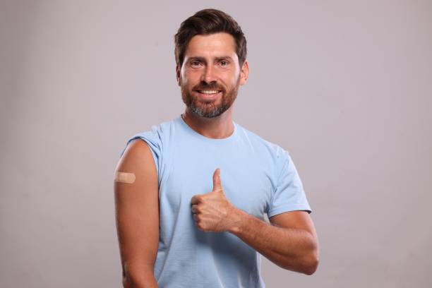 istock Man with sticking plaster on arm after vaccination showing thumbs up against light grey background 1893568665