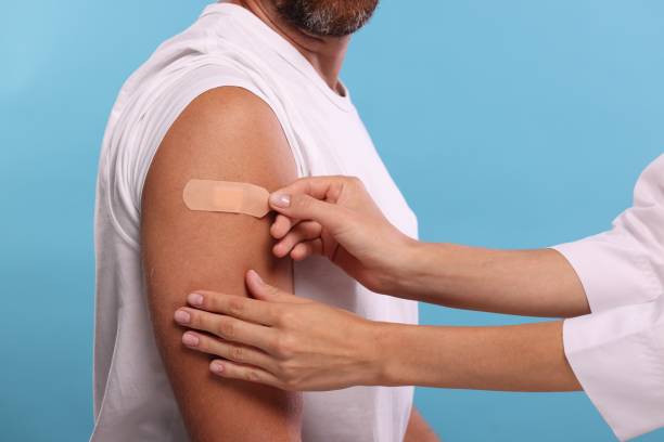 istock Nurse sticking plaster on man's arm after vaccination against light blue background, closeup 1893568670