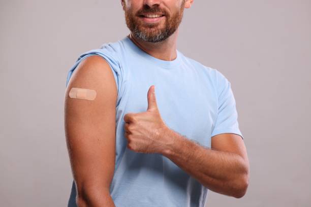 istock Man with sticking plaster on arm after vaccination showing thumbs up against light grey background, closeup 1893568676
