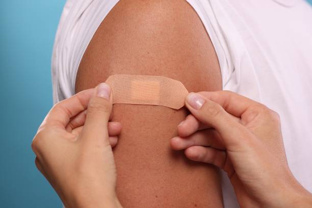 istock Nurse sticking plaster on man's arm after vaccination against light blue background, closeup 1893569702