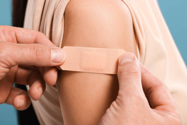 istock Doctor sticking plaster on woman's arm after vaccination against light blue background, closeup 1893572290
