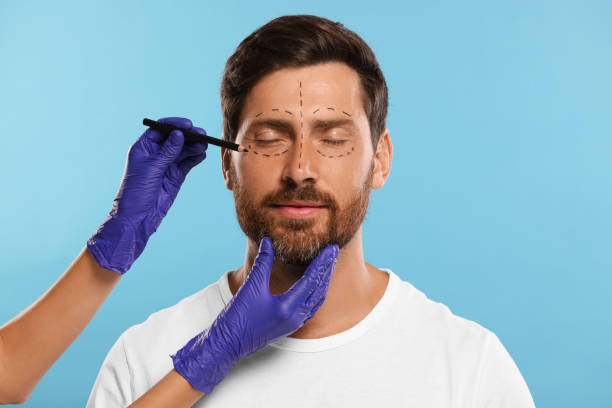 istock Doctor drawing marks on man's face for cosmetic surgery operation against light blue background 1893572796