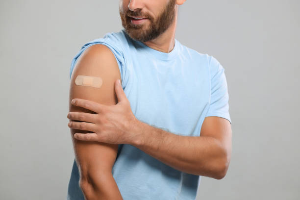 istock Man with sticking plaster on arm after vaccination against light grey background, closeup 1893575372
