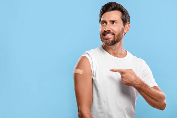 istock Man pointing at sticking plaster after vaccination on his arm against light blue background 1893575381